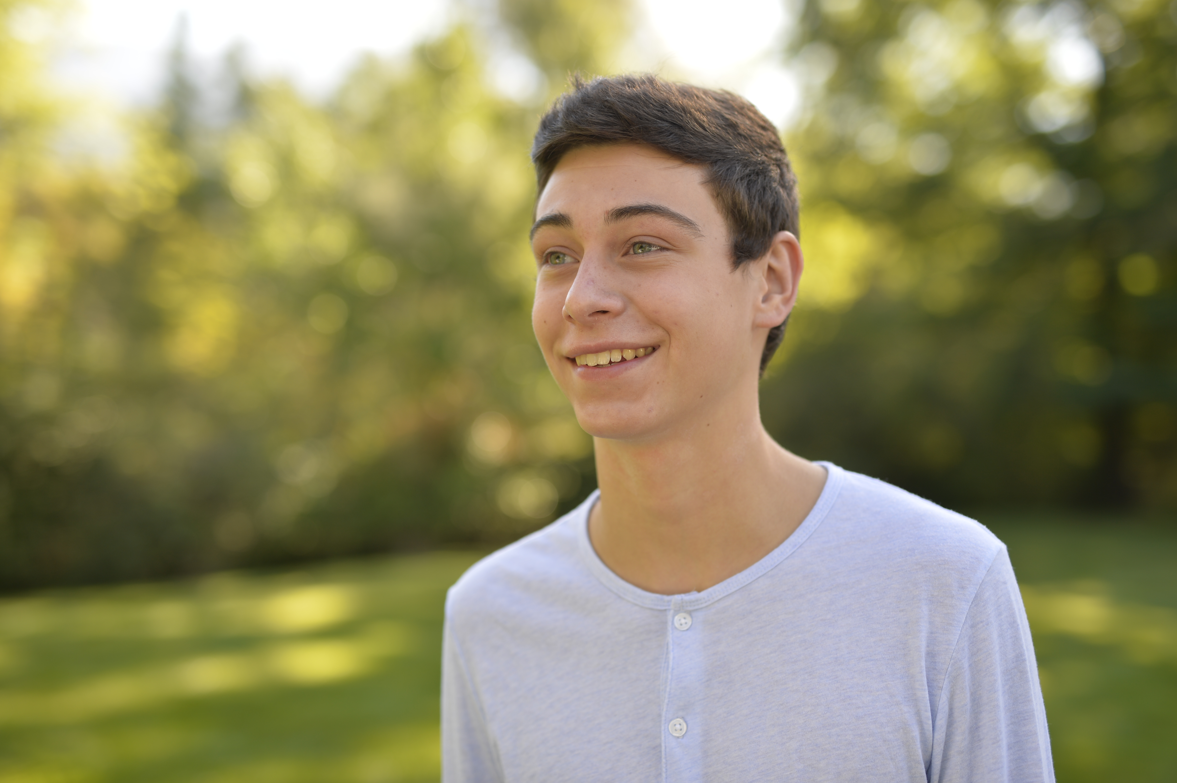 A young man walks around a park.  He looks like he is thinking or pondering.  Also shots of him sitting.